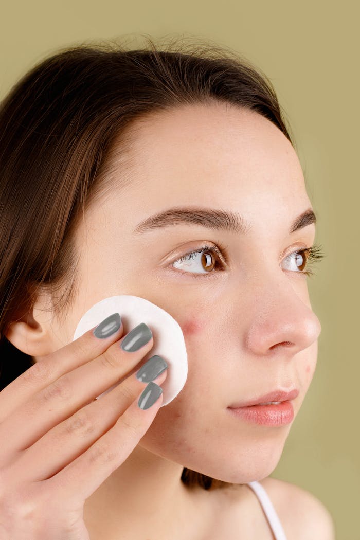 Young woman using a cotton pad on her face for skincare treatment, focusing on clarity.